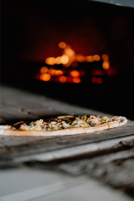Uncooked pizza on a wooden paddle beside a glowing wood-fired oven