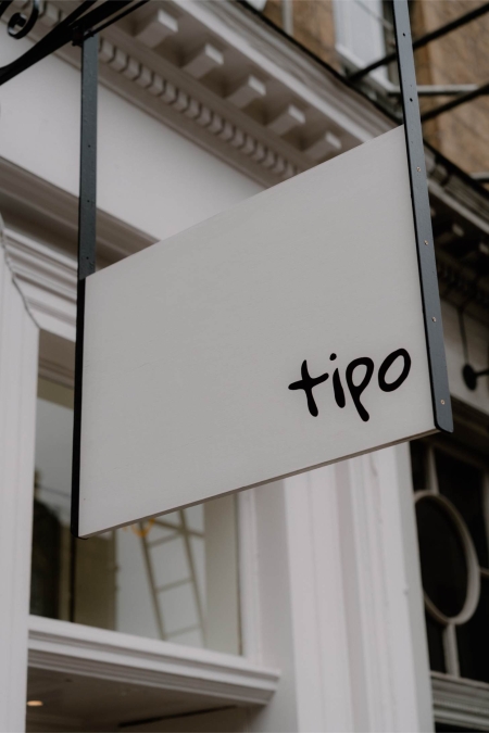 Blank white sign reading "tipo" hangs beneath a decorative building cornice