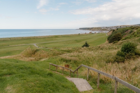 Wooden steps lead down through grassy dunes towards a curving coastal path