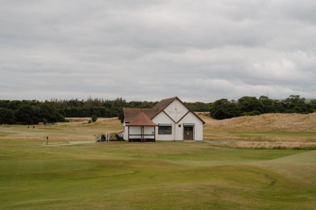 White clubhouse with red tiled roof beside a links golf course