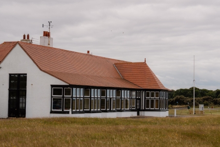 White clubhouse with red tiled roof and black-framed windows overlooking grassy links