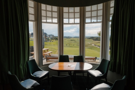Bay window overlooking a golf course, table and green chairs inside
