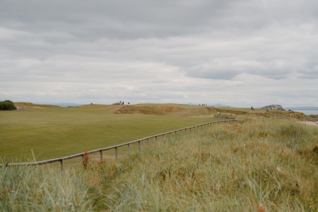 Wooden fence lining a coastal golf course fairway under grey skies