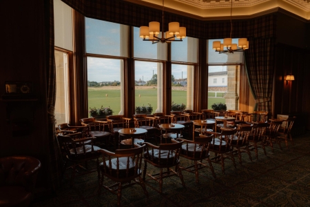 Wooden chairs and tables face bay windows overlooking a golf course