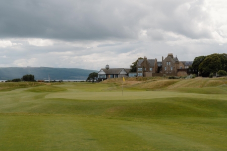Golf green with yellow flag before a clubhouse overlooking the Firth of Clyde