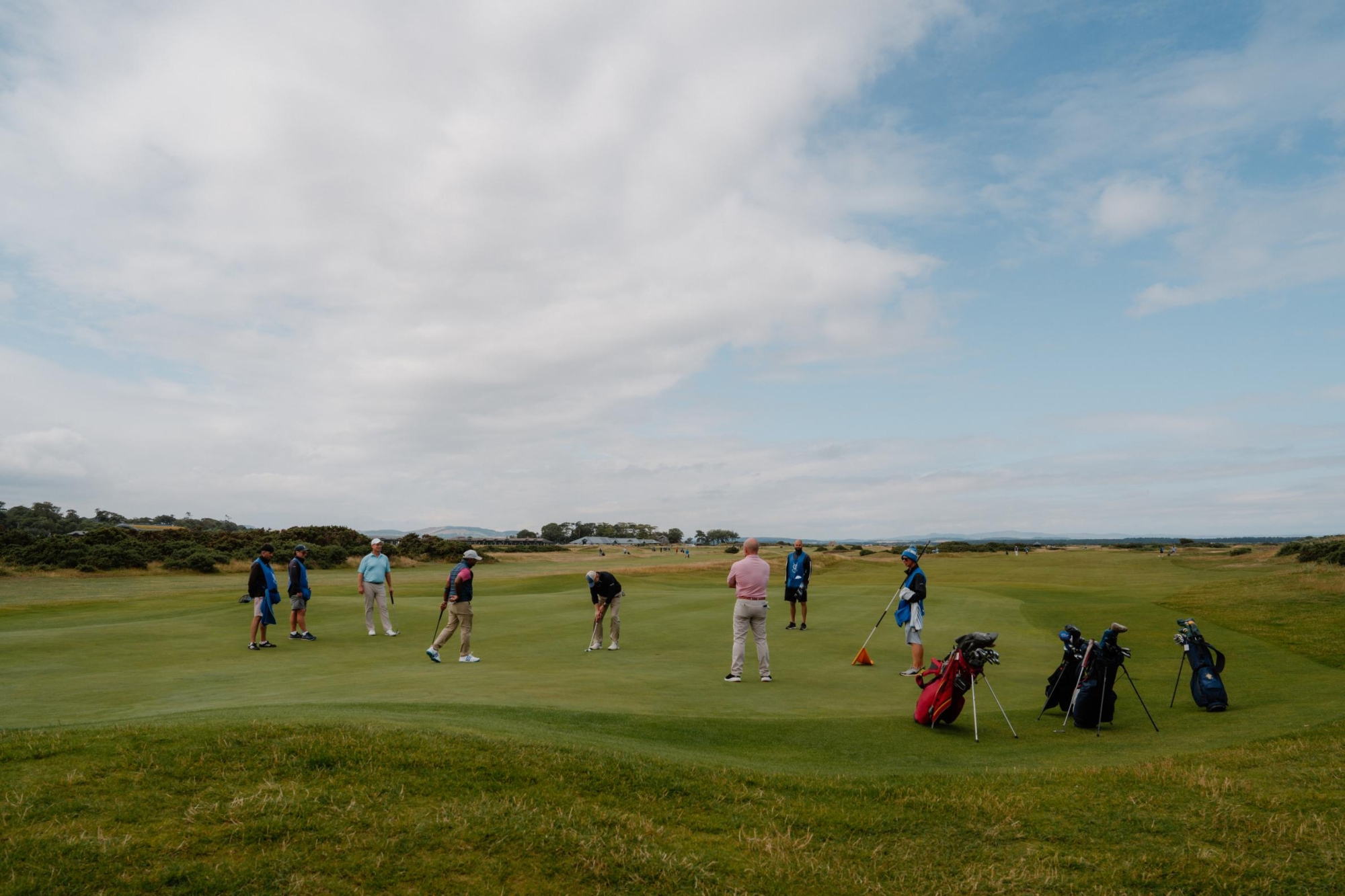 Golfers putting on a coastal links green under a wide cloudy sky