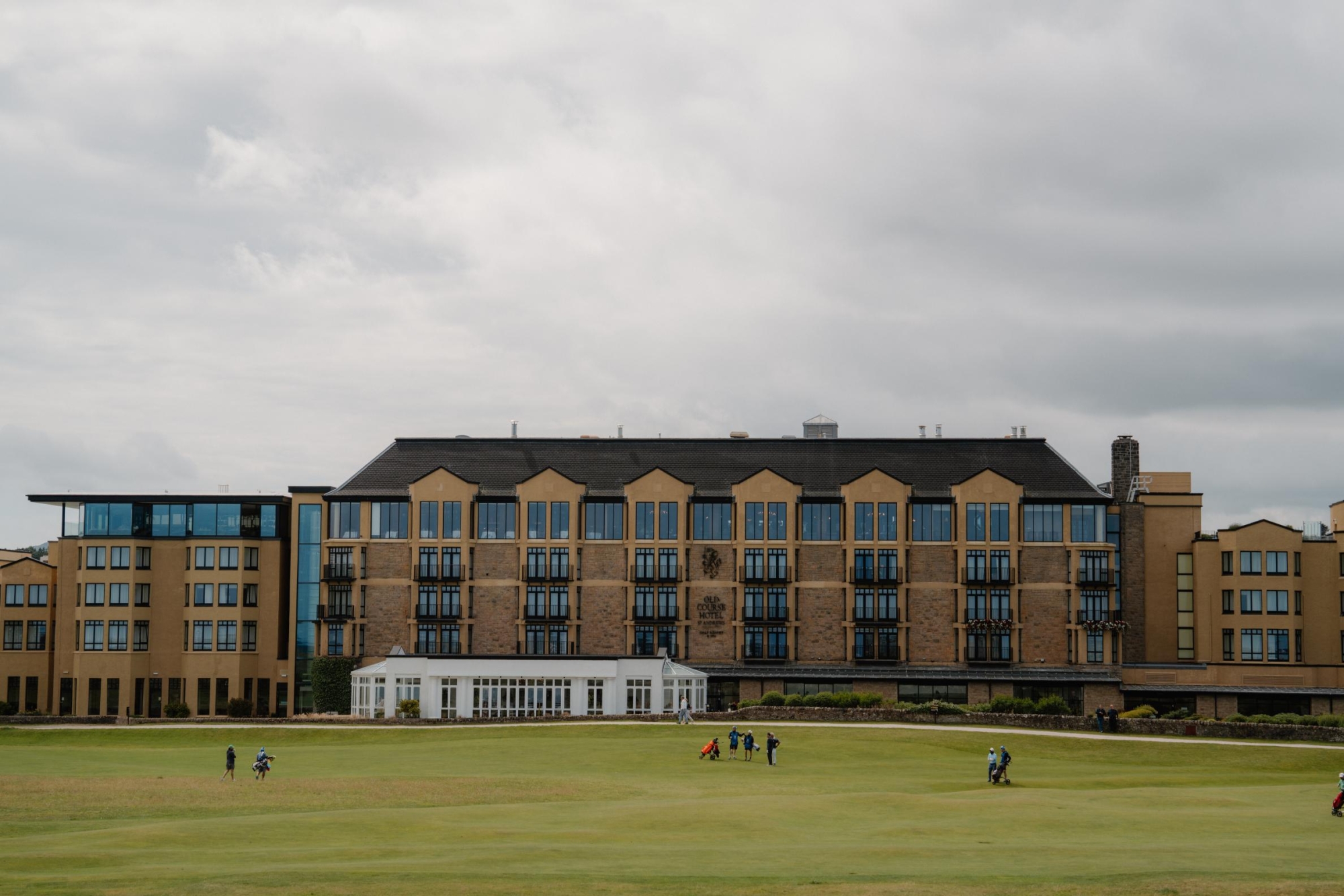 Golfers cross the green in front of a large sandstone hotel