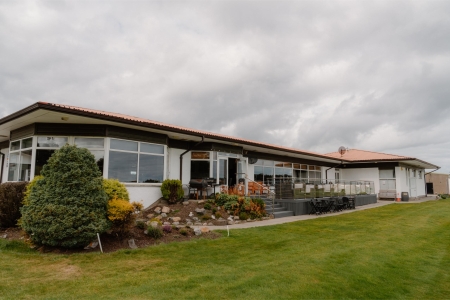 Single-storey clubhouse with terrace tables, rockery garden and lawn under grey skies