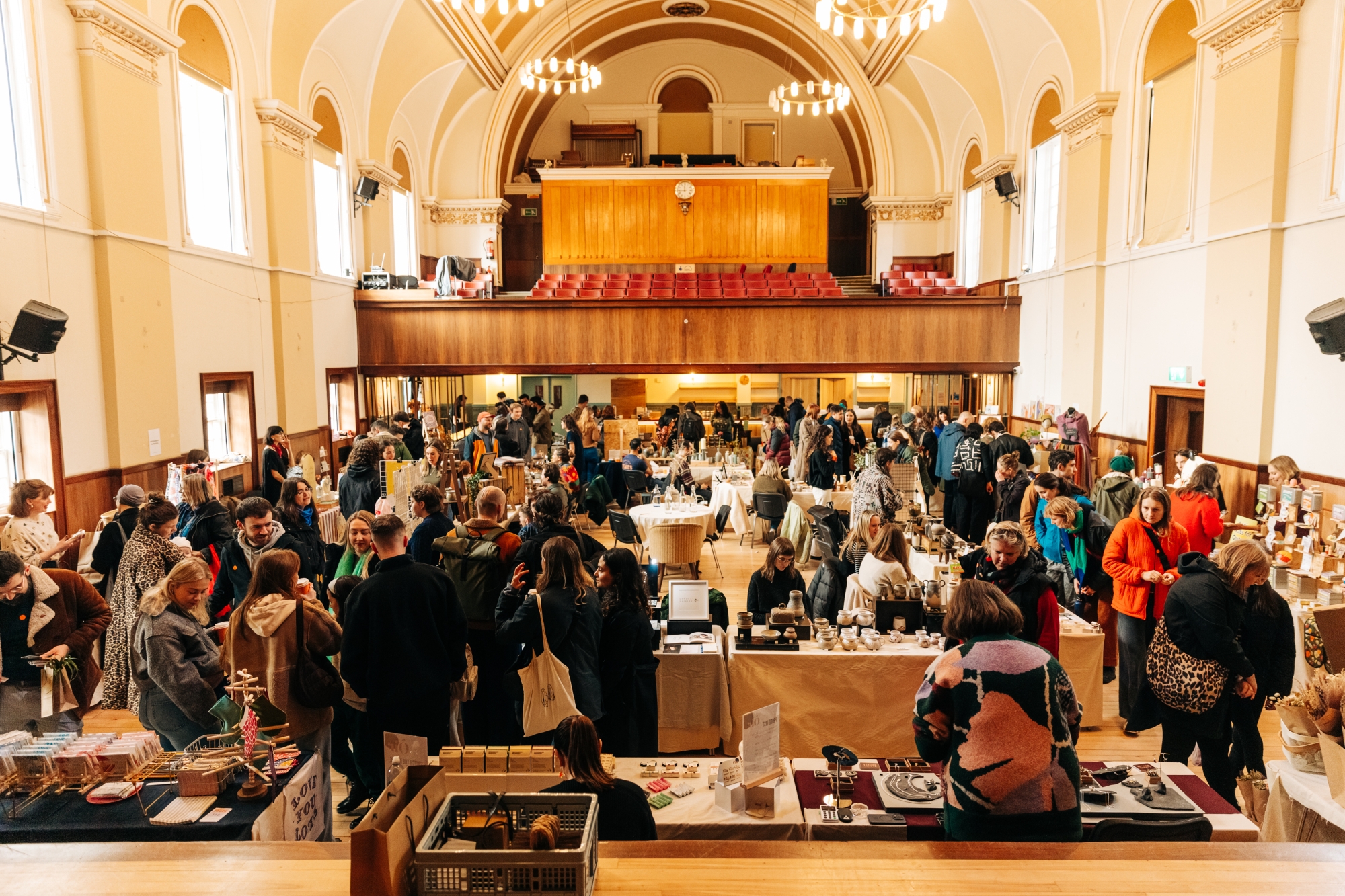 Crowds browse market stalls in a grand hall with balcony seating