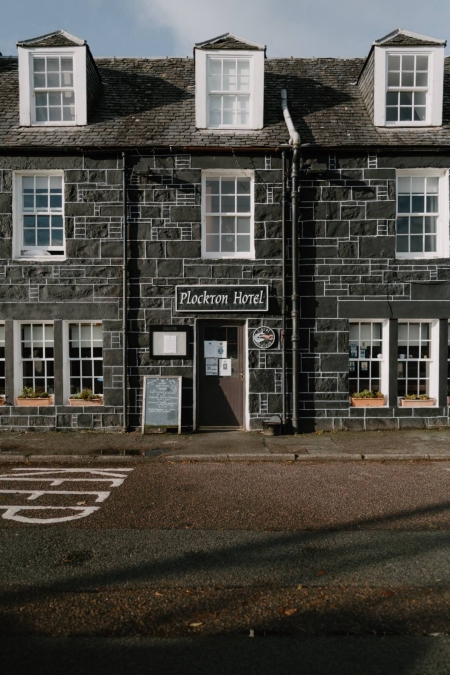 Stone-fronted Plockton Hotel with three white dormer windows and a red door