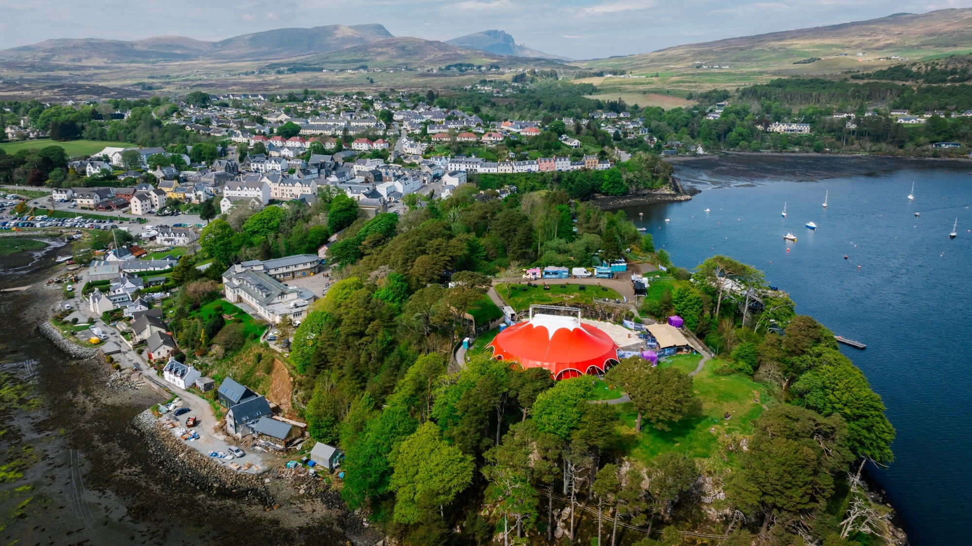 Aerial view of Portree's white houses and harbour with a red circus tent among trees