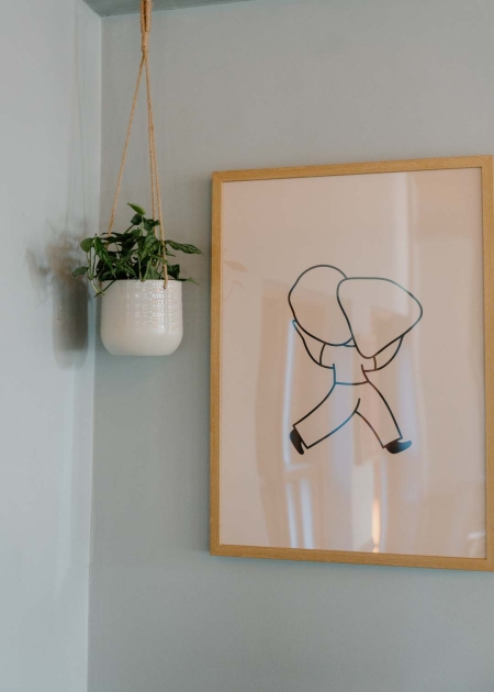 Framed line drawing beside a hanging plant in a white macramé pot