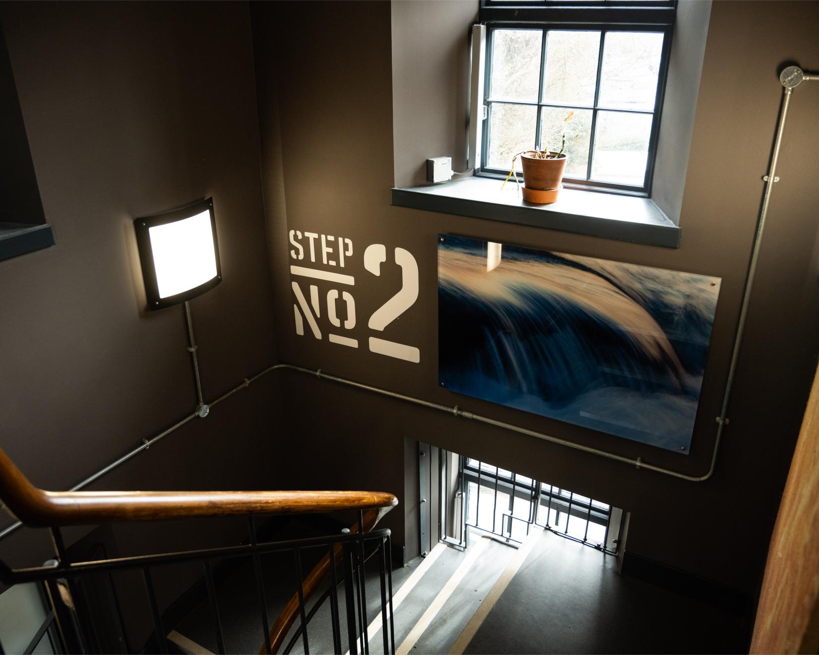 Stairwell with "STEP NO. 2" stencilled beside a waterfall photograph and windowsill plant