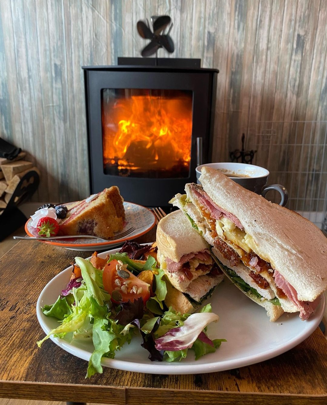 A toasted sandwich and salad by the stove at the Coffee Bothy, a slice of cake behind.