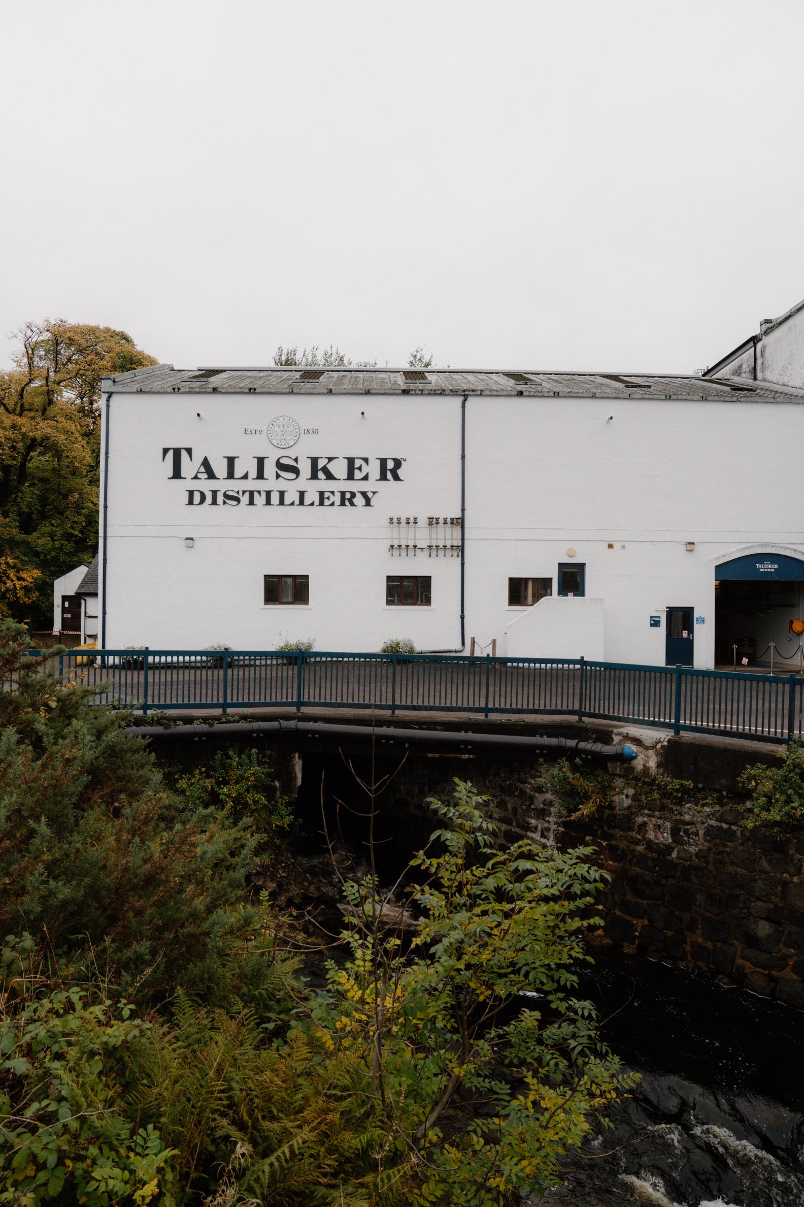 White painted building marked Talisker Distillery, with a footbridge crossing the burn below