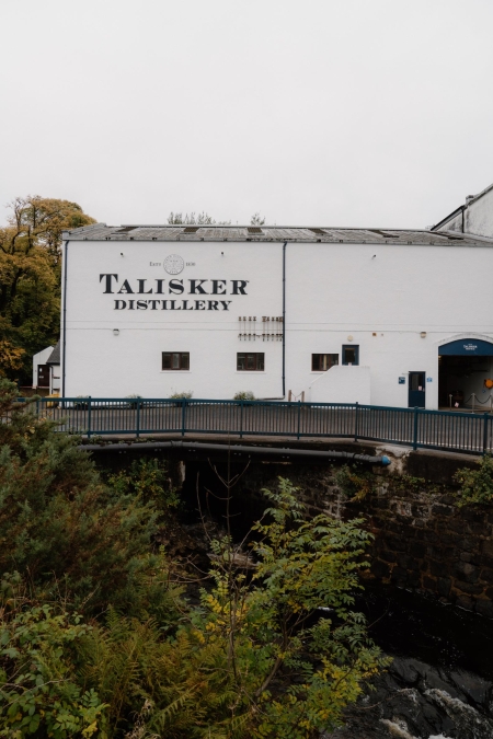 White painted building marked Talisker Distillery, with a footbridge crossing the burn below