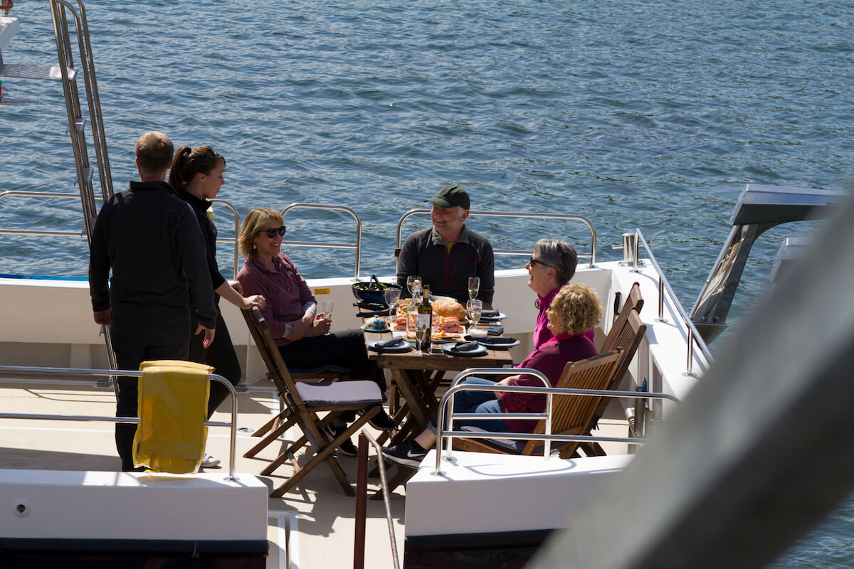 Guests round a table on Seaflower's open deck, the seafood lunch laid out between them.