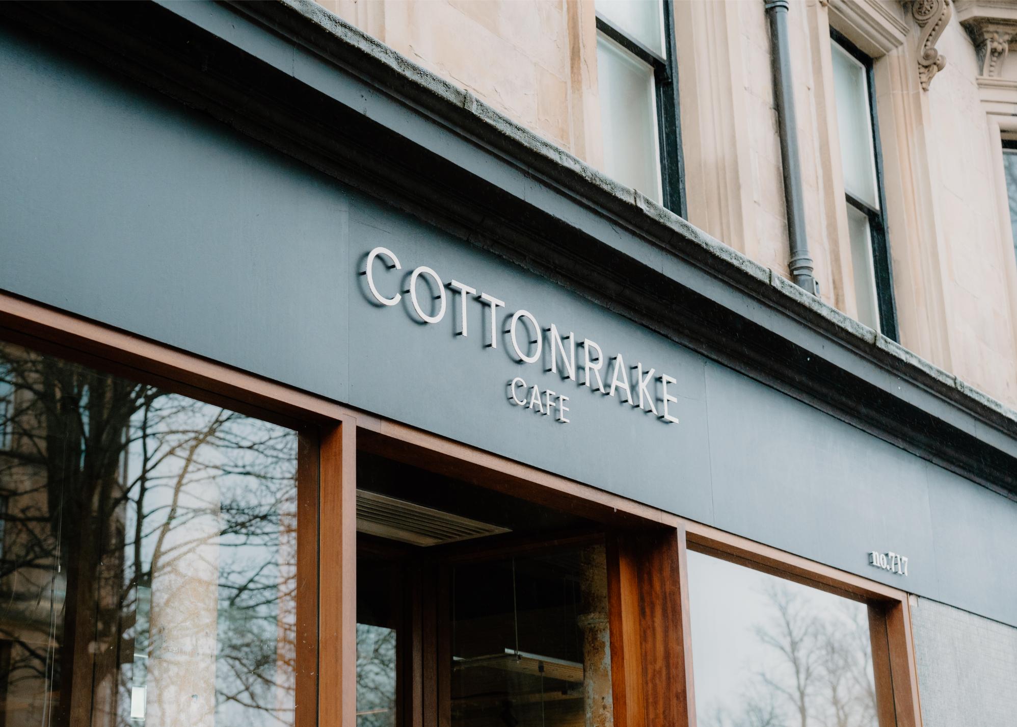 The Cottonrake Café fascia in grey above tall timber windows.