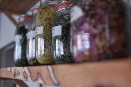 Glass jars of dried herbs and flowers lined up on a wooden shelf