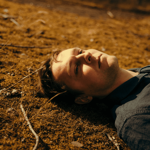 Man lying on dry moss and twigs, looking upward