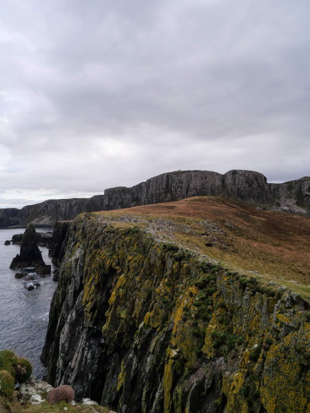 Lichen-streaked basalt cliffs above the sea at Rubha Hunish, a stack standing off the point.