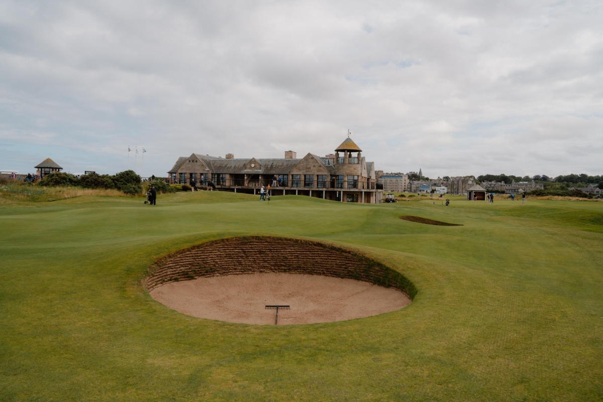 Golfers approach the clubhouse past a deep pot bunker on the fairway