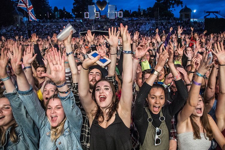 Festival crowd cheering with raised arms under evening stage lights