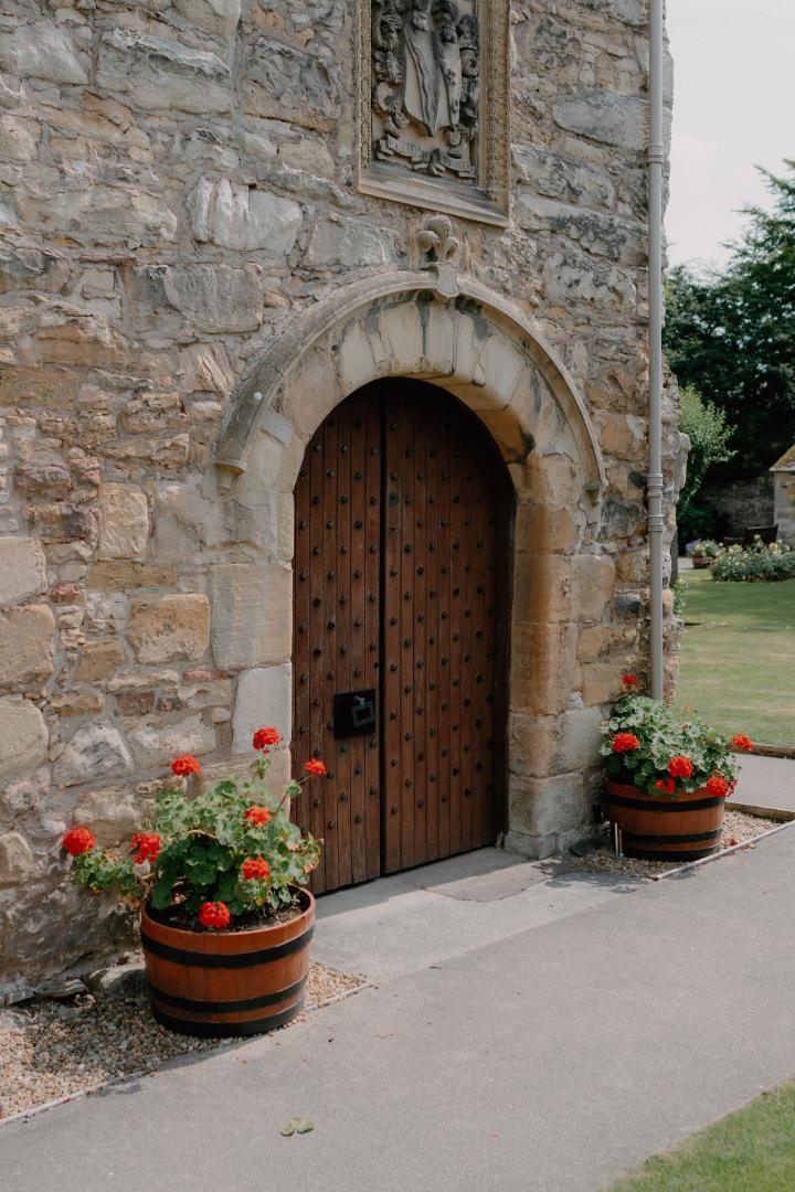 Arched wooden door in a stone wall, flanked by geranium barrels