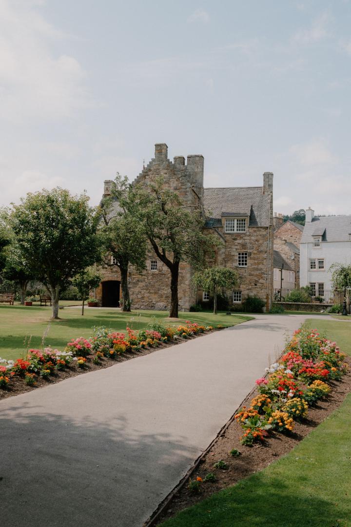 Stone tower house behind flowerbeds and a paved path in Jedburgh