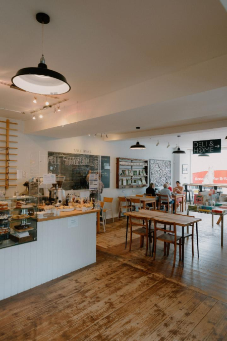 Café interior with wooden tables, chalkboard menu and a "Deli & Home" sign