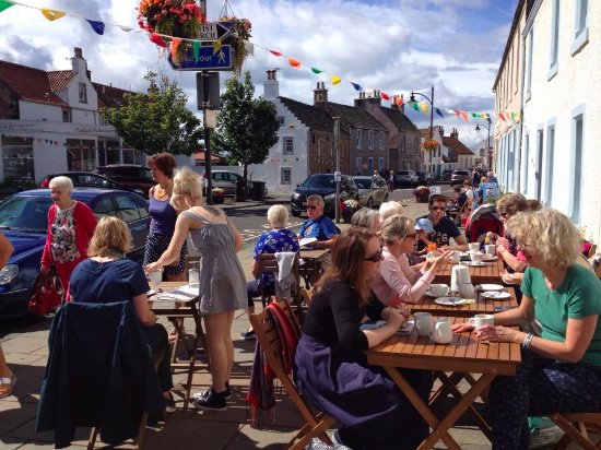 People sit at outdoor tables under bunting on a sunny high street