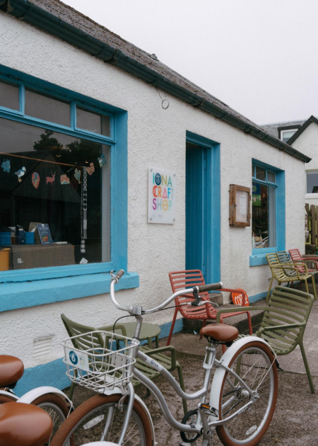 The whitewashed front of the Iona Craft Shop with blue window frames, bicycles and chairs outside.