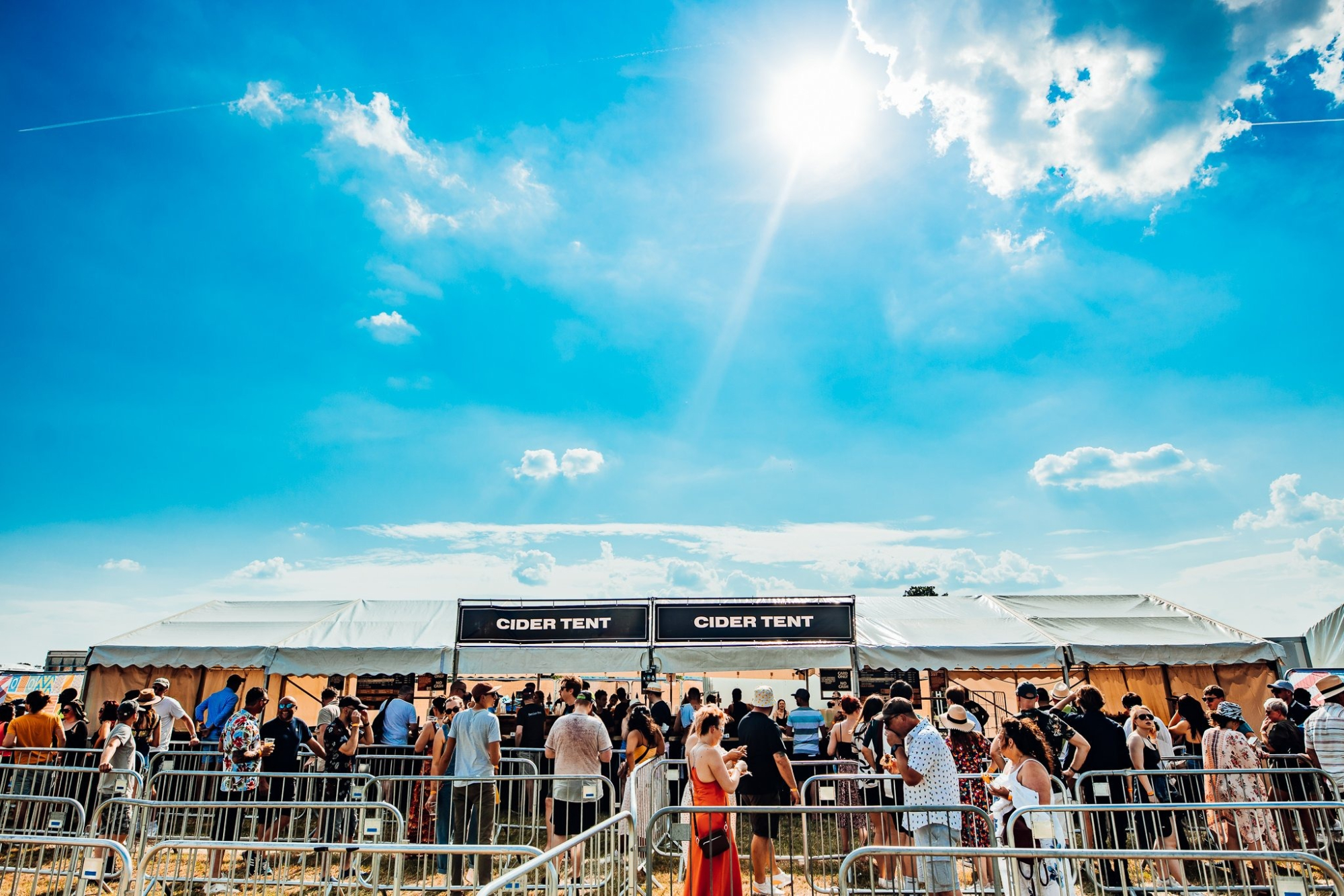 Crowds queue outside the Cider Tent under bright sunshine at a festival