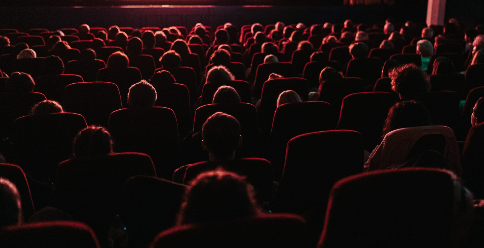 Rows of red cinema seats filled with an audience facing a lit screen