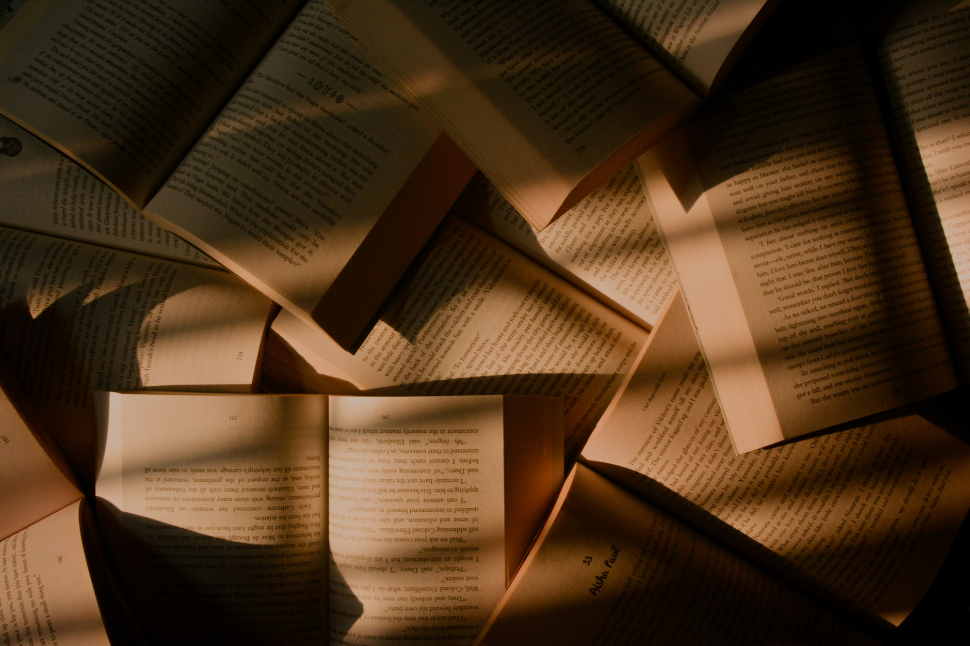 Open books scattered together, sunlight casting sharp shadows across their pages
