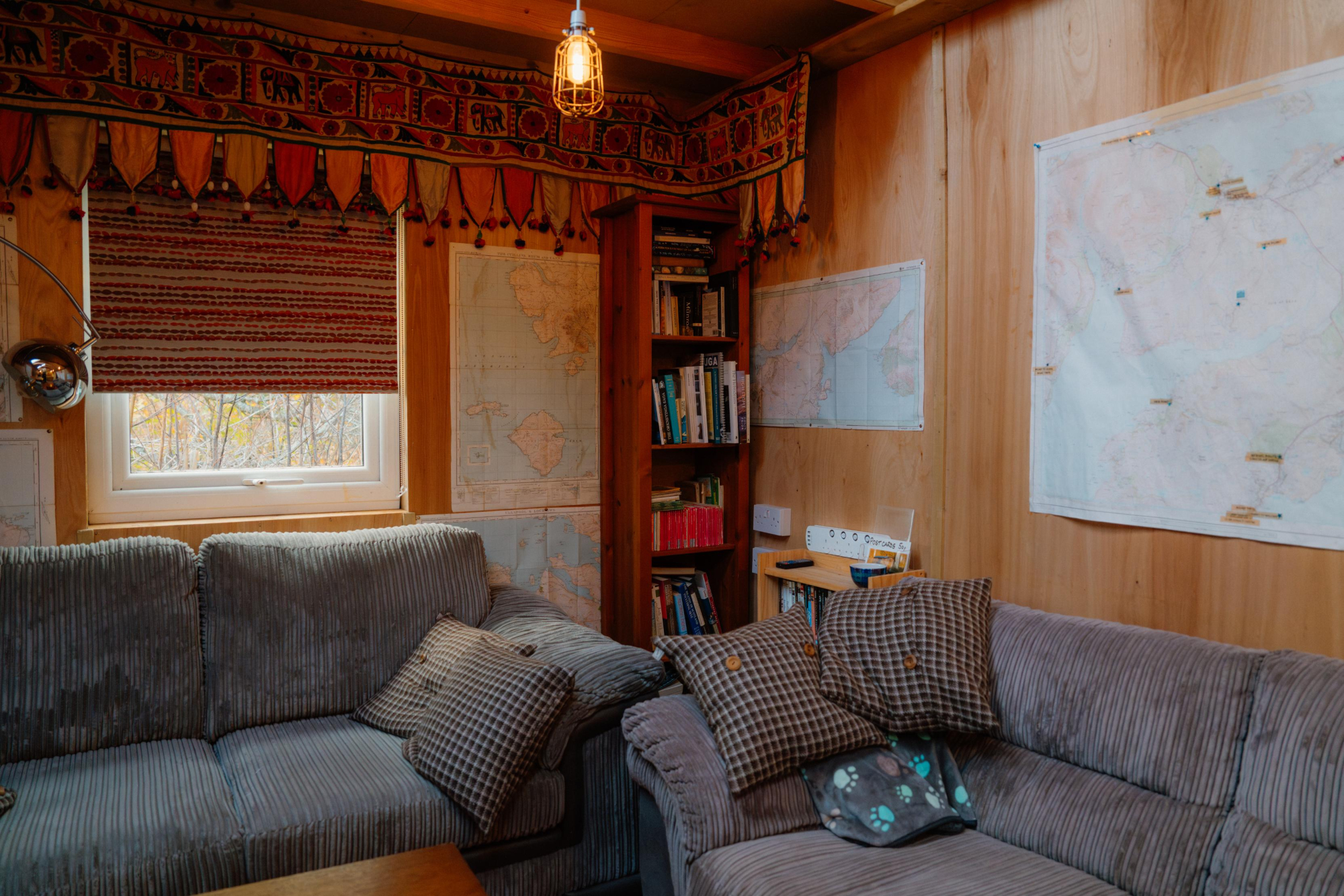 Two grey sofas with checked cushions face each other around a low table, maps pinned to the panelled walls and a bookshelf in the corner.
