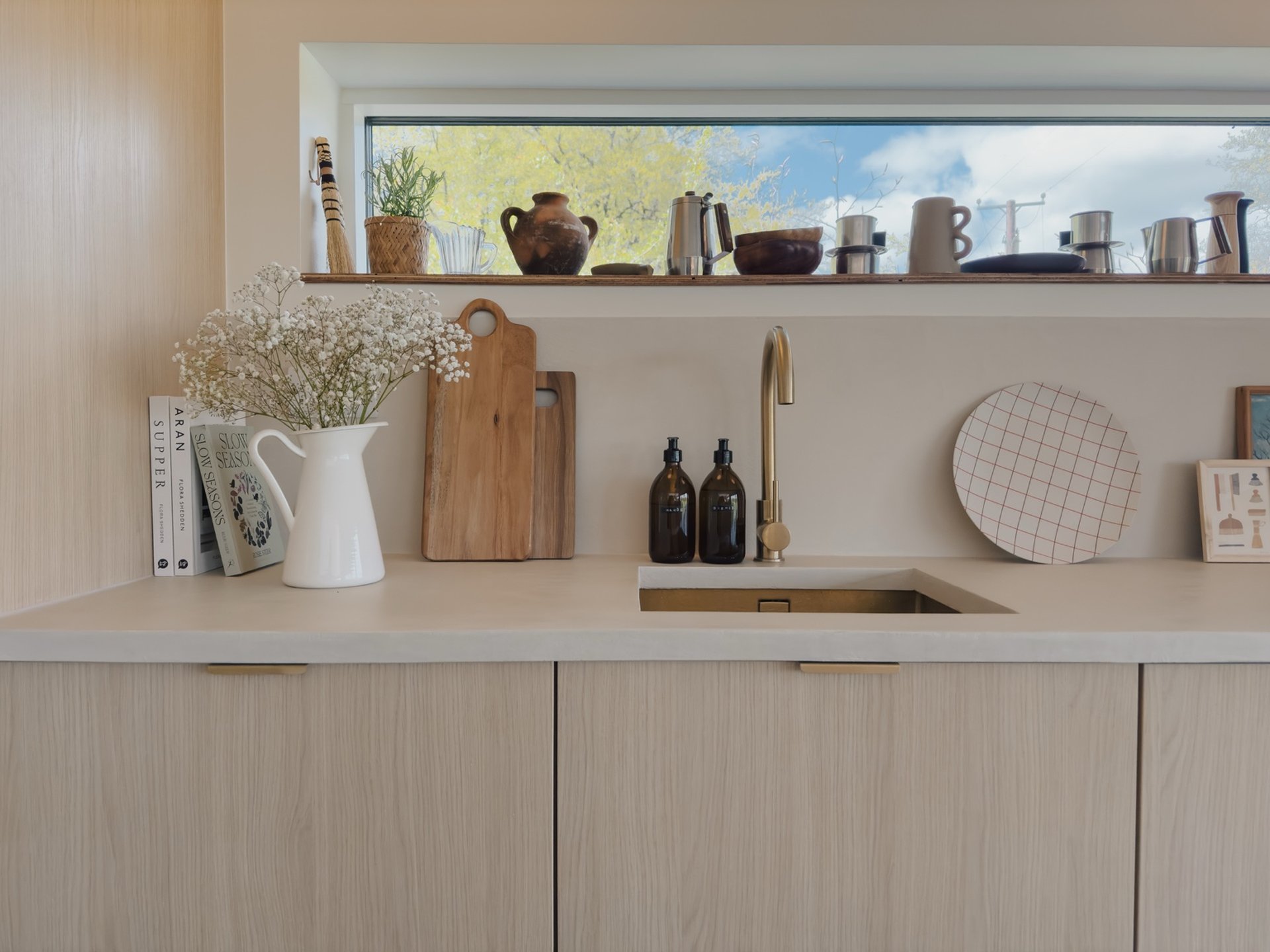 A jug of gypsophila and stacked books including "Casa" sit beside chopping boards on a kitchen counter, a brass tap and round tray to the right.