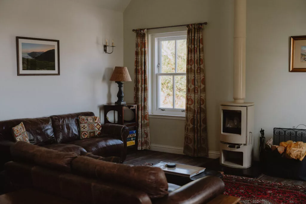 A leather corner sofa sits opposite a lit wood-burning stove, a patterned rug spread across the floor between them.
