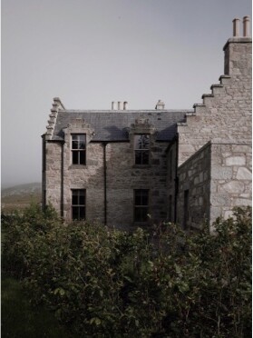 A grand stone house with crow-stepped gables stands among shrubs under a stormy sky, chimneys rising from its slated roof.
