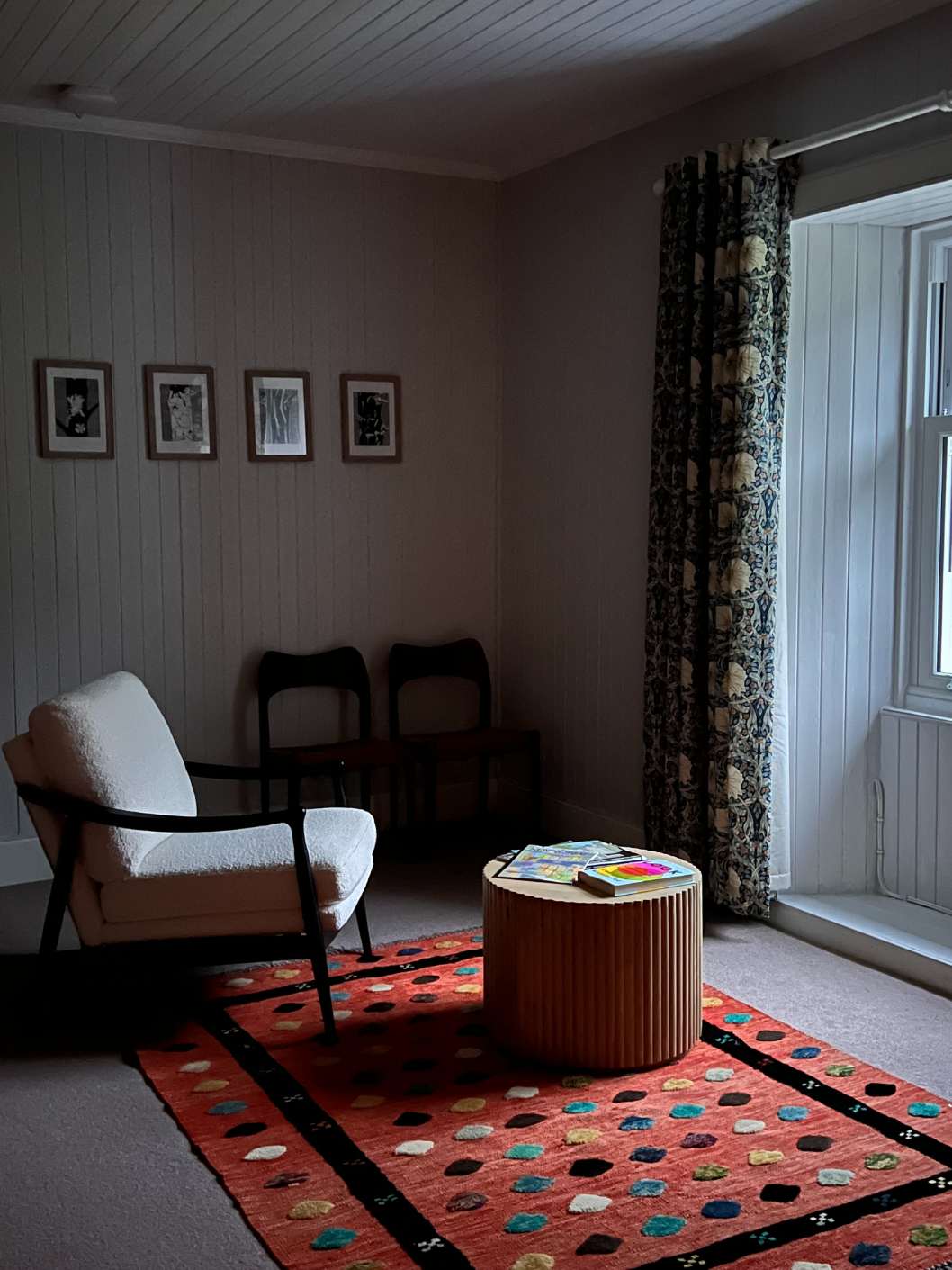 A blue wing-back armchair with a sheepskin throw sits in the corner of a terracotta-panelled room, a sofa draped with sheepskins and a patterned kilim rug in the foreground.