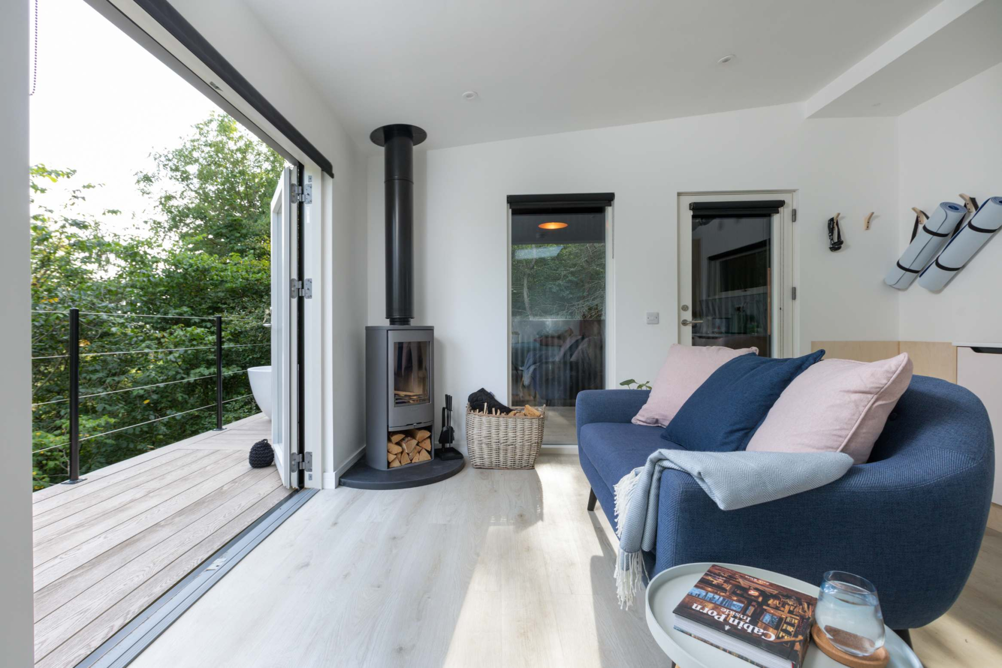 A living area with a wood burning stove and a blue sofa, glazed doors open onto a timber deck.