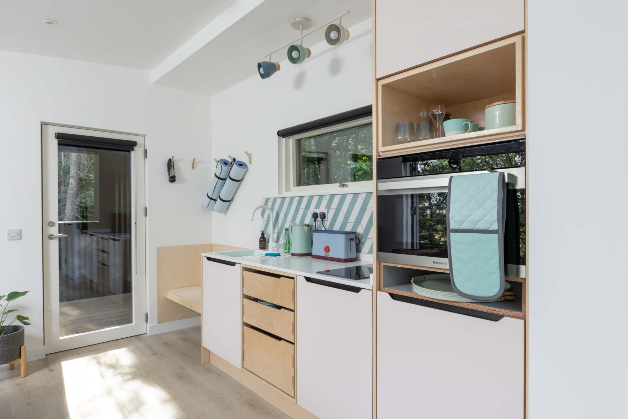 Kitchen units with open shelving holding mugs and glasses above a worktop with a built-in microwave and a toaster.