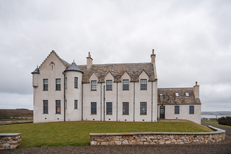 A turreted white mansion with stepped gables and tall chimneys stands behind a low stone wall on a lawn.