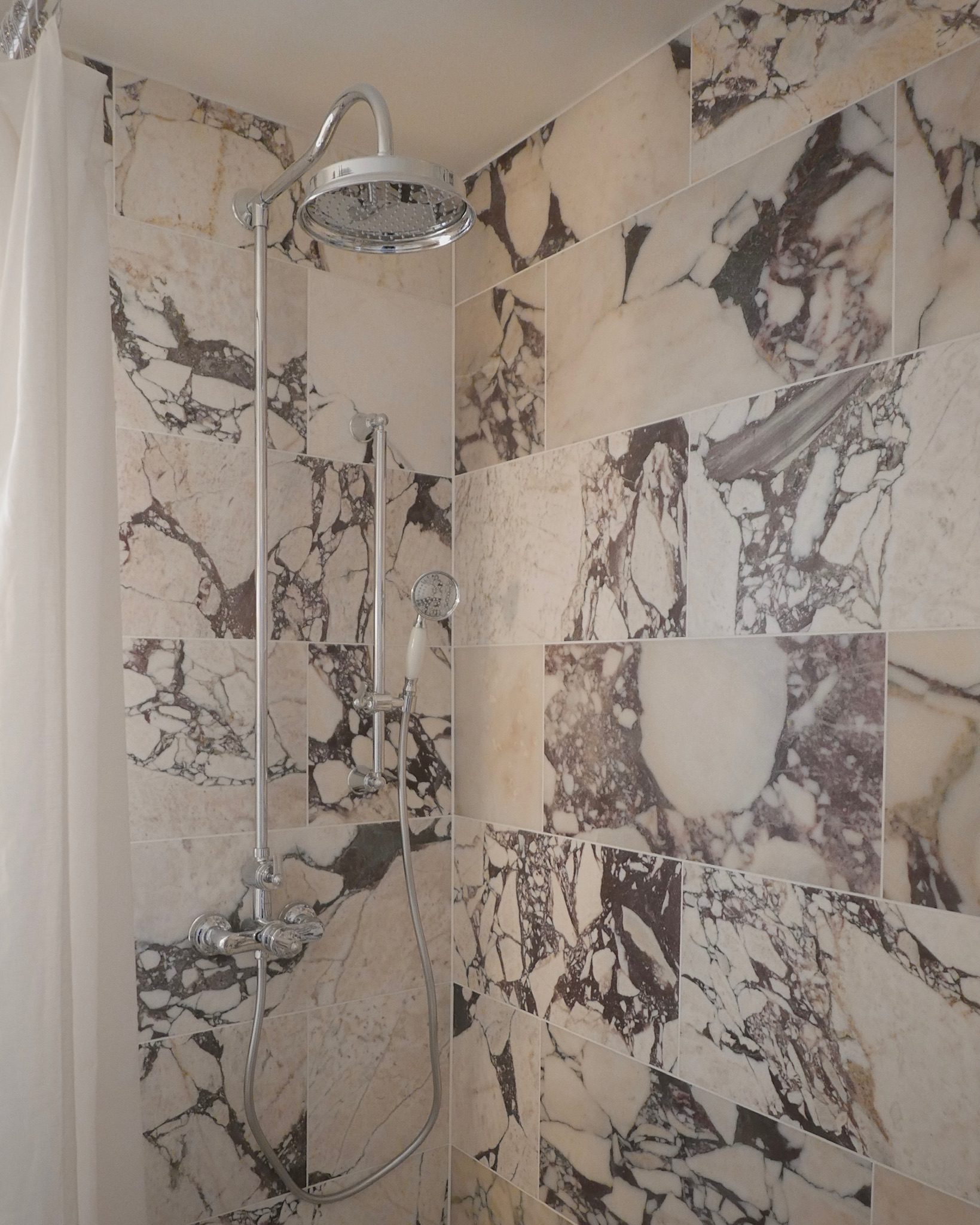 A rainfall shower head and handheld attachment are set into a marble-effect tiled shower cubicle.