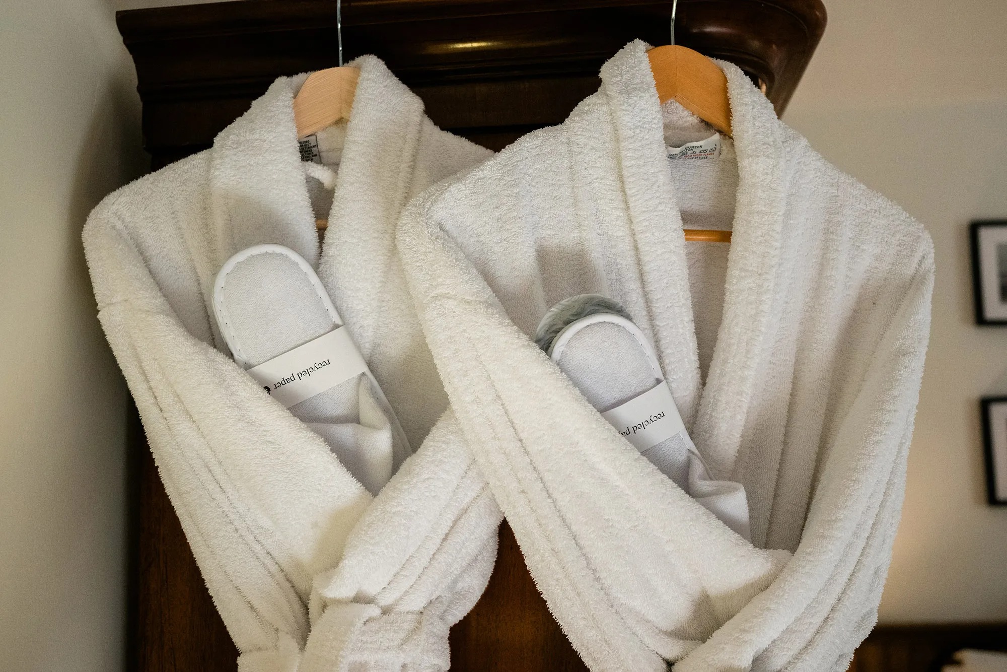 Two white robes hang from a dark wooden wardrobe, slippers tucked into the pockets.