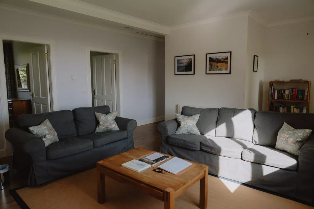 Two grey sofas with patterned cushions face each other around a wooden coffee table, framed prints and a bookcase along the far wall.