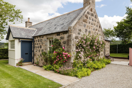 A stone cottage with a slated roof and a blue front door, climbing roses in pink and white flanking the porch.