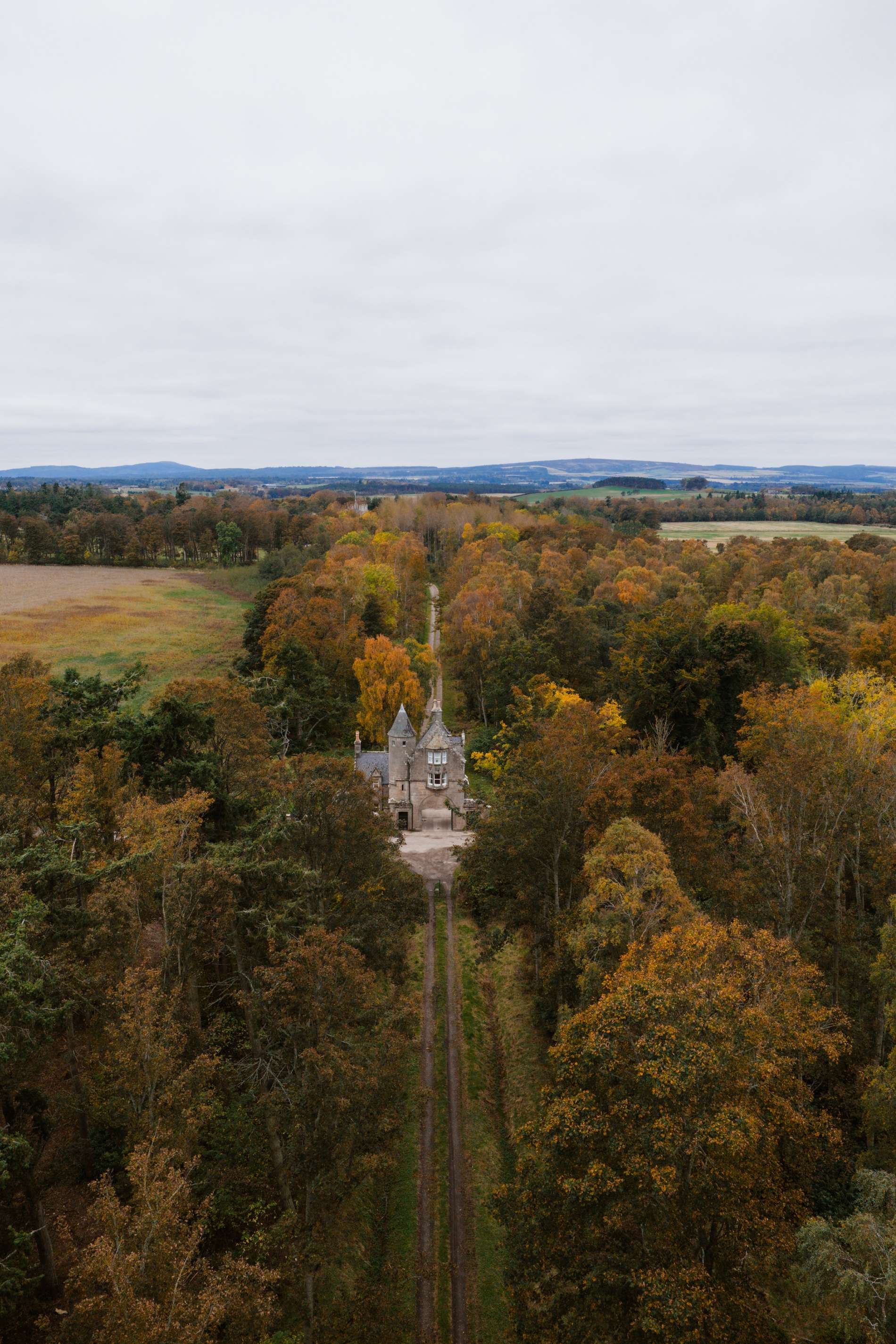 An aerial view shows the stone gatehouse at the end of a tree-lined avenue, fields and hills stretching into the distance.