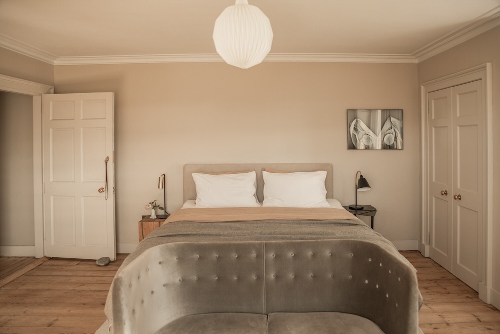 A bed with pale linen sits between two panelled doors, a framed abstract print on the wall and a paper lantern light above.