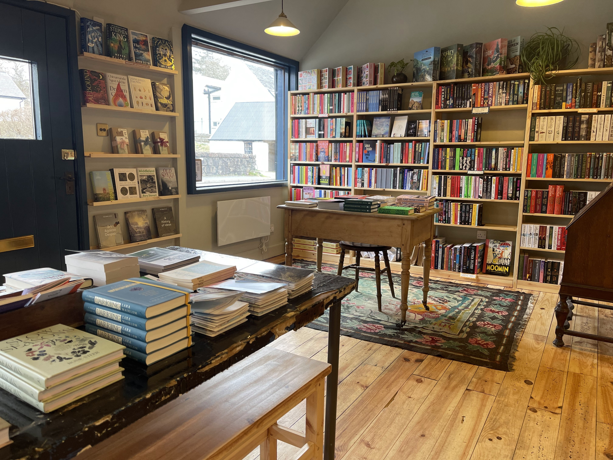 Tables of new books and a rug in Waystone Books, shelves to the ceiling behind.